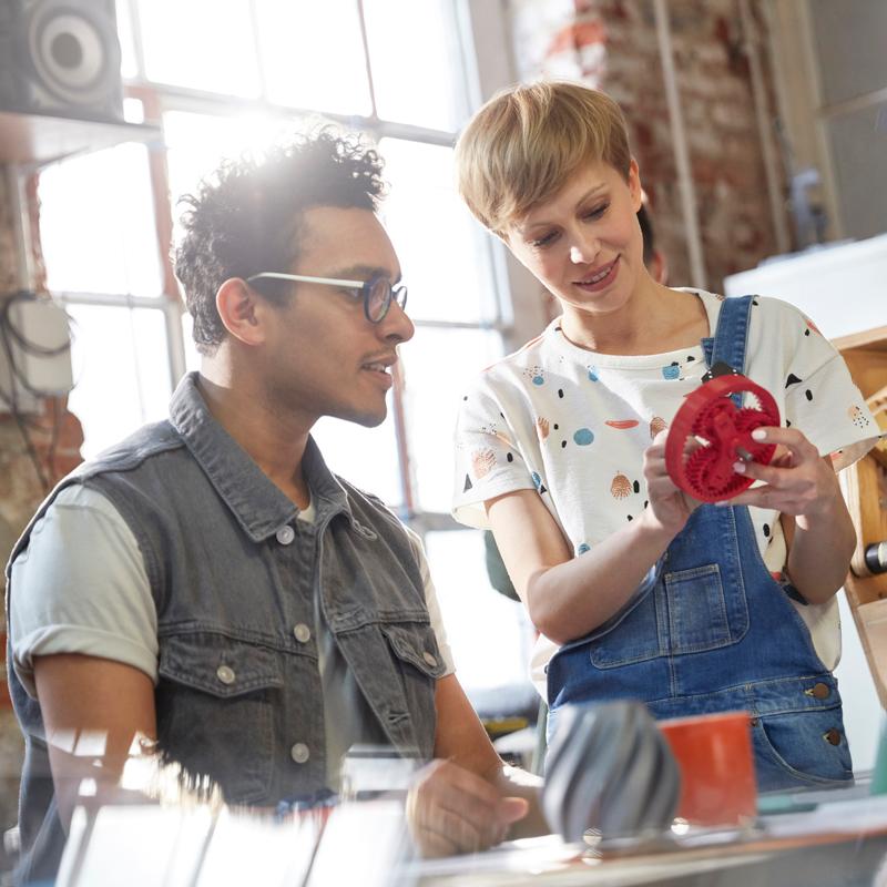 Man and woman in shop looking at 3d printed gear