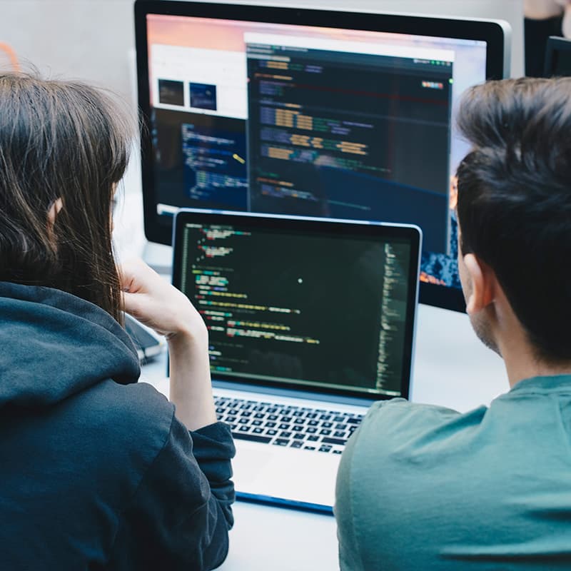 Two developers looking at a laptop screen as well as a desktop screen