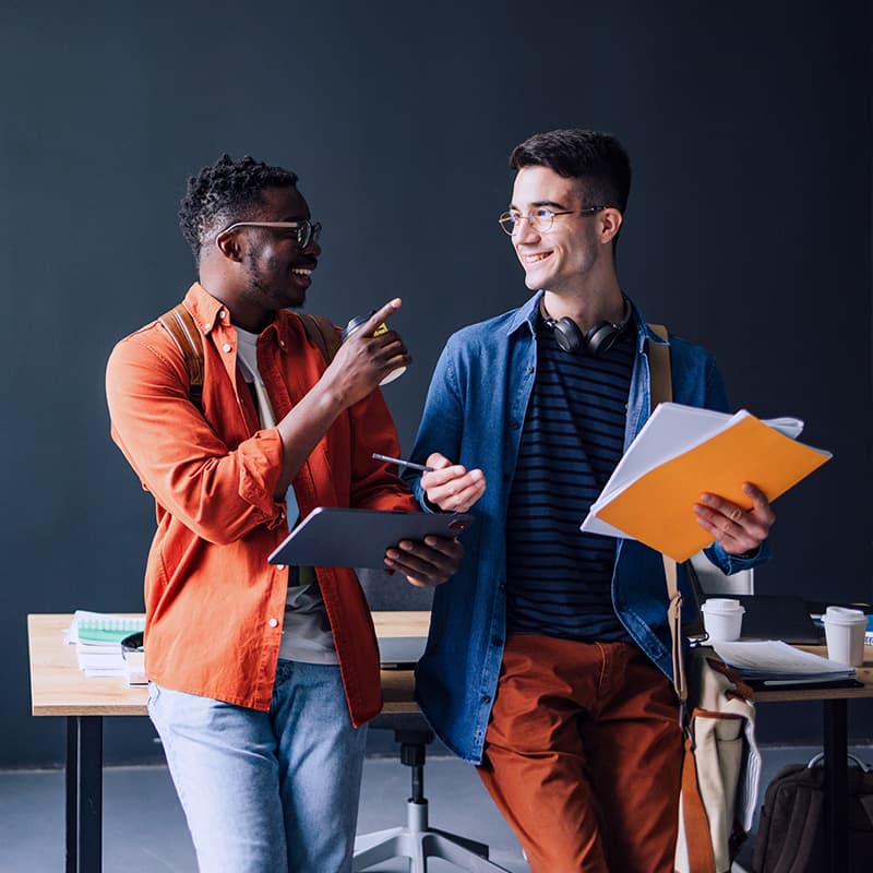 Two colleagues in a discussion holding a tablet and paper while leaning on a table