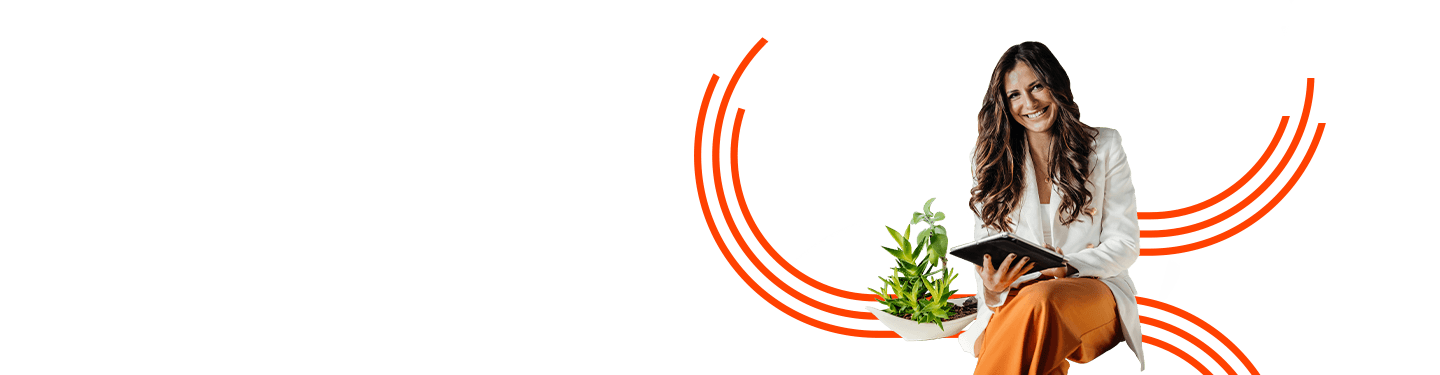 A woman wearing white business jacket and orange trousers, sitting on a desk with a desk plant next to her, looking at GreenLine Ricoh Remanufactured Products on her tablet.