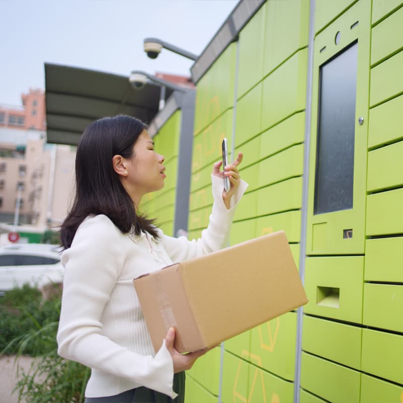 Woman holding a package in front of smart locker screen and holding her phone up to it