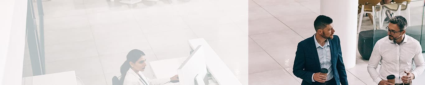 Two men walking in an office with a woman working at a desk