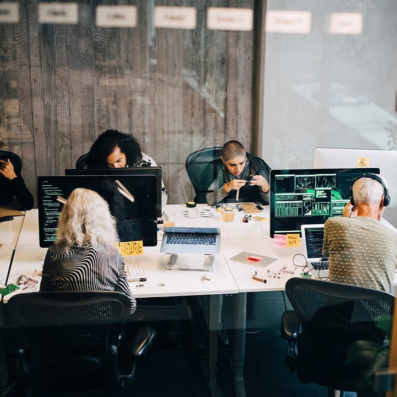 Team of developers working at their shared table using laptops and desktops