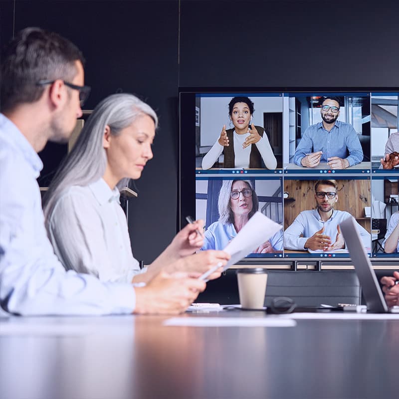 videoconference in meeting room with people sitting in modern office and colleagues on big screen monitor. Business technologies concept.