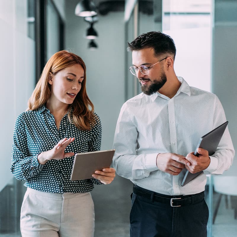 A woman showing how to drive growth with detailed metrics and reporting on a tablet to a man holding a laptop.